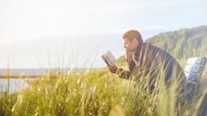 A man reading a Bible sitting on a park bench.