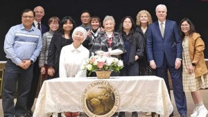 a group of people standing behind a table with a white cloth, floral arrangement and UCG seal