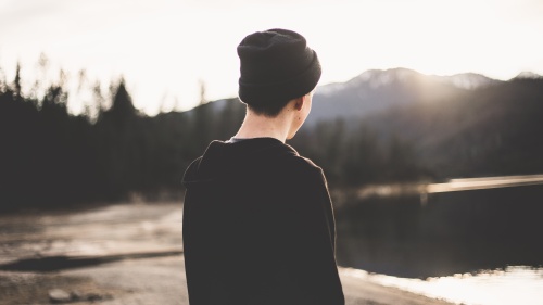 a boy facing away from the camera towards a landscape of water, sand and hills