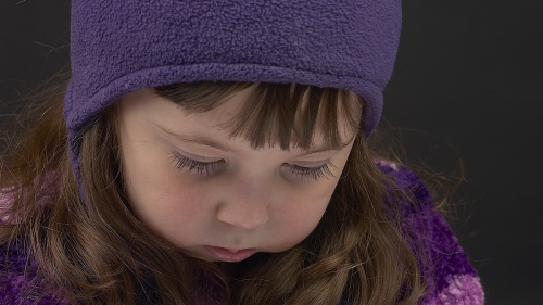 A little girl with a sad expression on her face looking down.