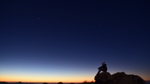 Uma pessoa sentada numa pedra ao pôr do sol.