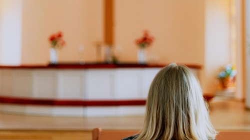 Uma mulher num banco de uma igreja olhando para o altar e a cruz.