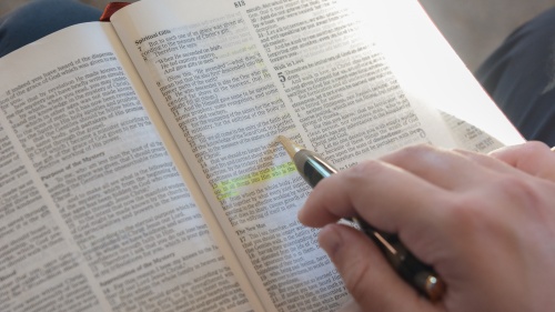 A photo of a hand highlighting a scripture in the Bible. 