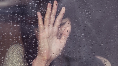 A woman behind a rain covered window.