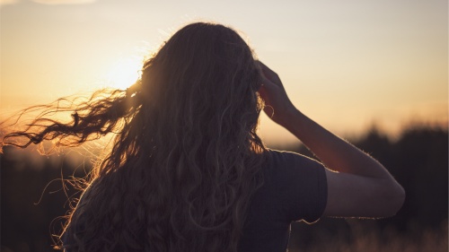 A woman looking at a setting sun.