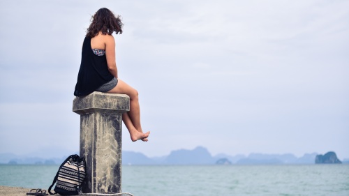 woman sitting on post looking at water