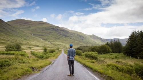 A young man walking on a paved hiking or biking path.