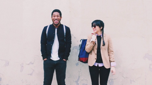 Two young adults waiting for a bus - both with smiles on the faces.