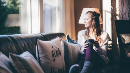 A young woman sitting on a couch looking out a window.