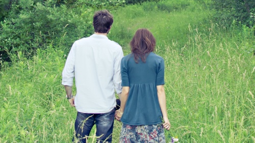 A young married couple holding hands standing in a grass field.