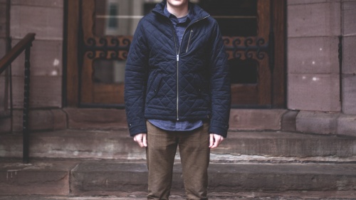 A man standing in front of an old building with steps leading up to big doors.