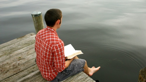 A man sitting on a dock reading a Bible.