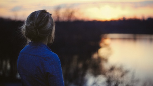 A young woman looking at the sun setting over water.