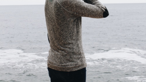 A woman standing by the ocean with hand on head.