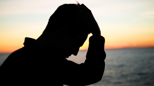 A silhouette of a man with his hand on his head.