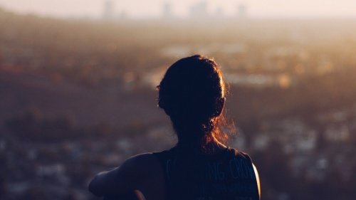 A woman sitting by herself on a cliff looking out over the town. 