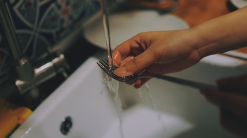 A woman washing a fork in a kitchen sink.