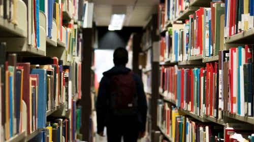 A person walking in a library surrounded by stacks of books.