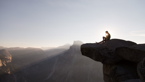 A man sitting on the edge of mountain cliff thinking.