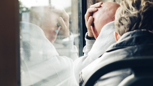 A man leaning up against a window holding his head.