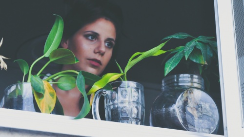 A woman looking outside a window with plants on the ledge.