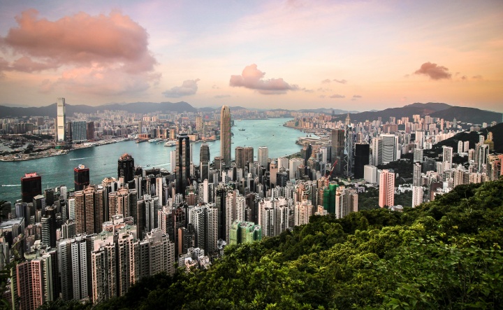 a city with green trees on the outskirts, skyscrapers and buildings, and a body of water running through the center.