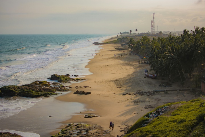 a shoreline with water and waves on one side and sand and greenery on the other