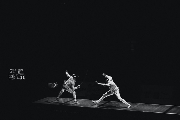 Two fencing partners sparring against a black background