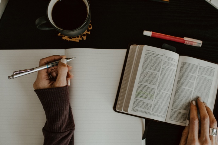 Woman's hands at a table with a notebook and a Bible