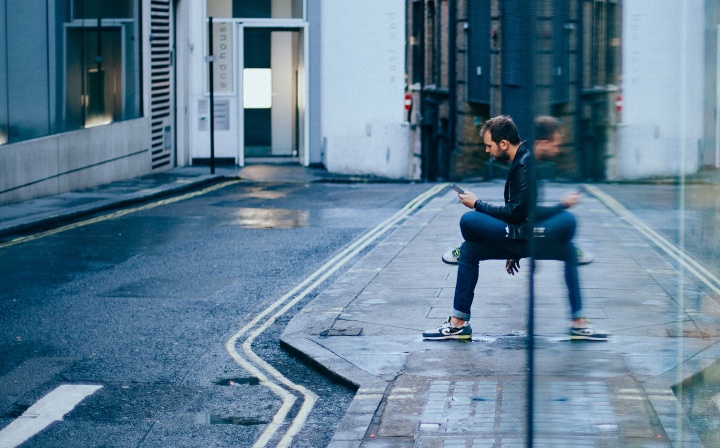 A man sitting by a building looking at his phone.