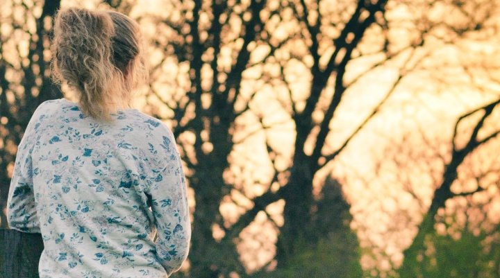 A woman outside looking a trees while the sun is setting.