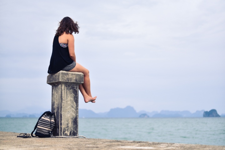 woman sitting on post looking at water