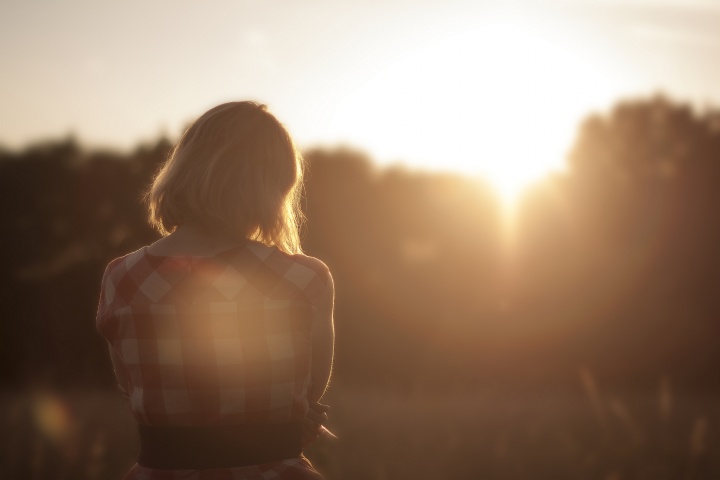 Woman standing in sunset with head down. 