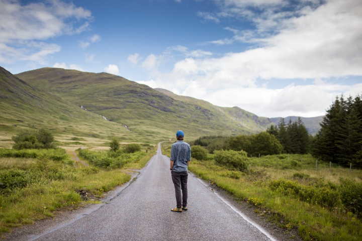 A young man walking on a paved hiking or biking path.