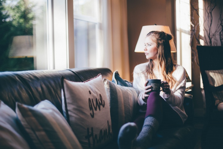 A young woman sitting on a couch looking out a window.