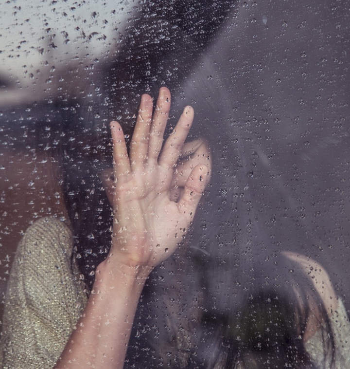 Woman with her hand up standing behind a window.