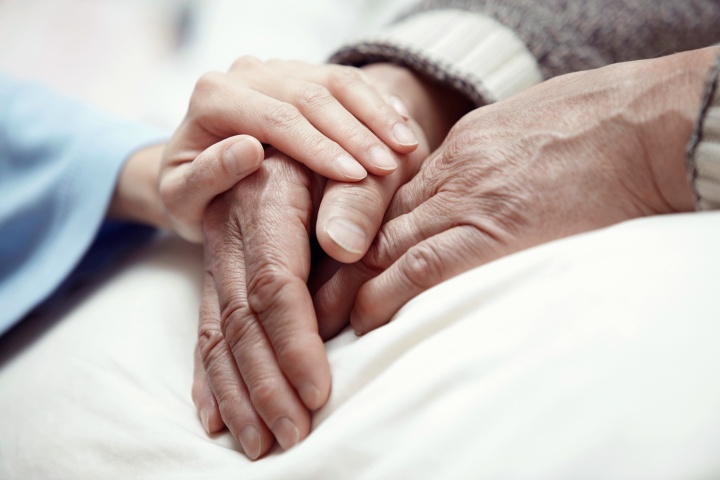 A young pair of hands comforting an elderly hand.