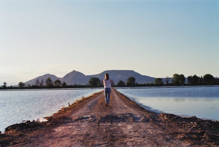 A woman walking on a path between two bodies of water.