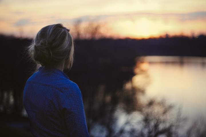 A young woman looking at the sun setting over water.