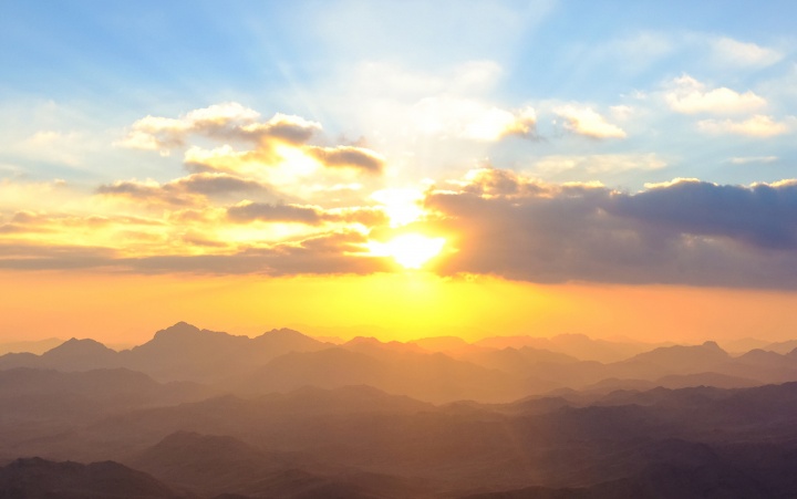 Sunset over a mountain range with clouds in the foreground.