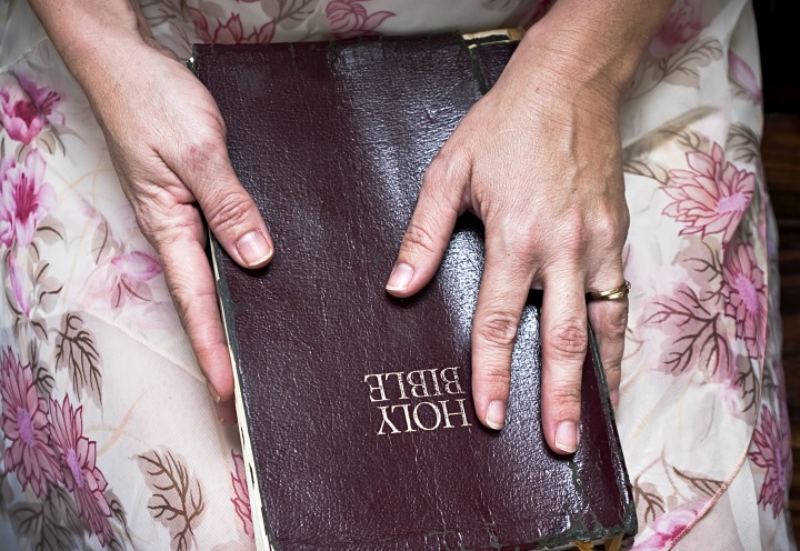 A Bible resting on the lap of a woman. Her hands on on top of the Bible.