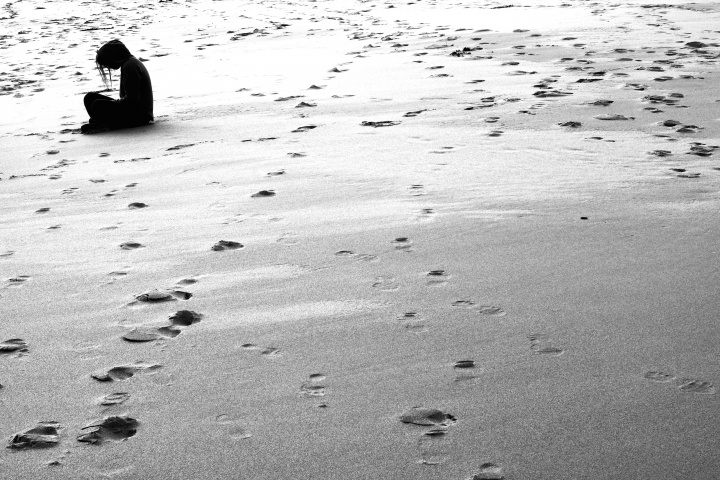 A woman sitting on deserted beach.