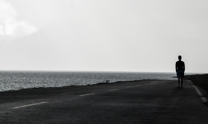 A man walking on a road beside a body of water.