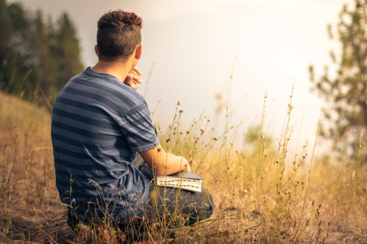 a man sitting outdoors in a field with an open Bible in his lap