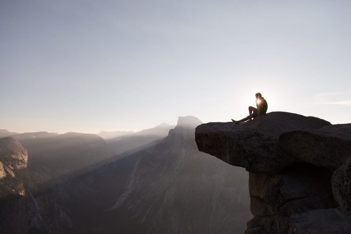 A person sitting on a cliff with sunset behind.