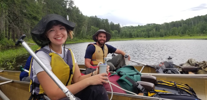 Two campers filter drinking water from the lake using a pump. 