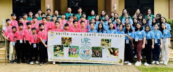 a large group of people standing outside in matching shirts with a UYC banner