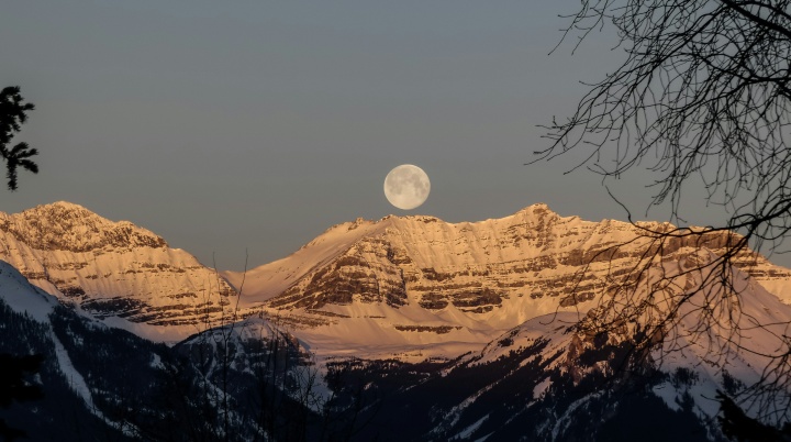 a full moon over a mountain range