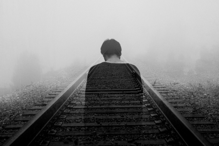 Photo of depressed man on railroad tracks.